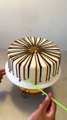 someone is decorating a cake with white and brown icing on a plate while holding a green toothpick