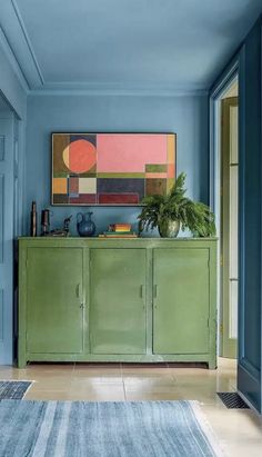 a blue room with a green cabinet and rug on the floor, in front of a painting