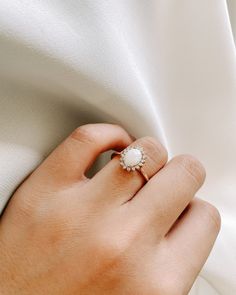 a woman's hand with a diamond ring on her left hand and white fabric in the background