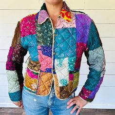 a woman standing in front of a white wall wearing a jacket with colorful patches on it