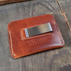 a leather wallet with a metal money clip on it's front pocket, sitting on a wooden surface