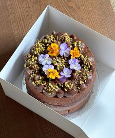 a chocolate cake with flowers on top in a white box, ready to be eaten