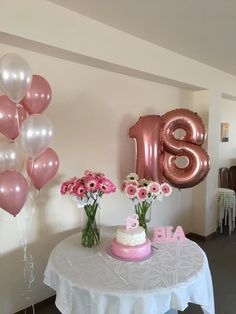 a table topped with pink and white flowers next to a number eighteen balloon filled with balloons