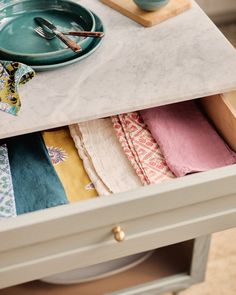 an open drawer with folded towels and napkins on it, next to a bowl