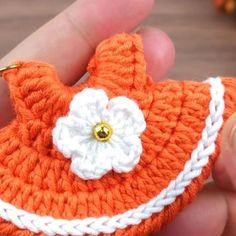 an orange crocheted purse with a white flower on the front and side, being held by a person's hand