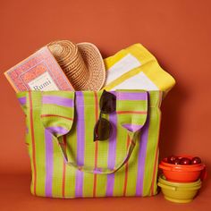 a green and purple striped tote bag with sun glasses, straw hat, and other items