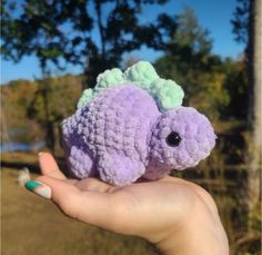 a hand holding a small purple and green crocheted elephant