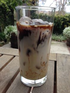 an iced drink with donuts in it sitting on a wooden table next to some bushes