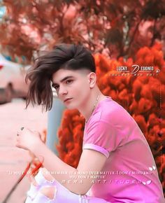 a young man sitting on top of a sidewalk next to red flowers in the background