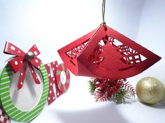 two christmas decorations hanging from strings on a white surface with ornaments around them and a red ornament in the middle