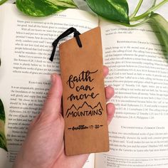 a bookmark with the words faith can move mountains on it and a hand holding an open book