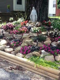 a garden with rocks, flowers and a statue in the backround near a house