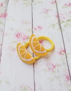 two yellow crocheted lemon slices are sitting on a white wooden surface with pink flowers