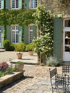 an outdoor table and chairs in front of a building with green shutters