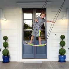 a young boy is swinging on a rope in front of a white house with blue doors