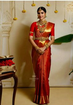 a woman in a red and gold saree standing next to a table with flowers