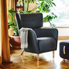 a chair with a blanket on it sitting in front of a window next to a potted plant