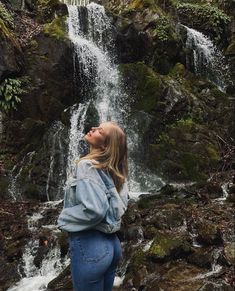 a woman standing in front of a waterfall with her eyes closed and head tilted to the side