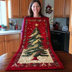 a woman holding up a quilted christmas tree on top of a wooden table in a kitchen