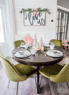 a dining room table set for four with green chairs and christmas decorations on the wall