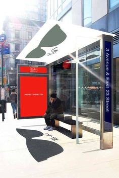 a man sitting on a bench in front of a bus stop next to a building