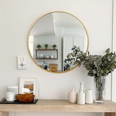 there is a mirror on the wall above a table with vases and other items