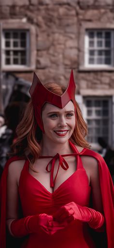 a woman in a red dress and cape smiles at the camera