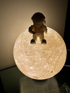 a small toy is sitting on top of a table lamp that looks like an astronaut's body