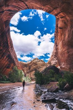 a man is walking in the middle of a river under an arch shaped rock formation