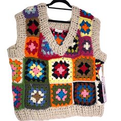 a multicolored crocheted sweater hanging on a hanger with a tag