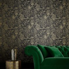 a green couch sitting in front of a black wallpapered room with gold accents