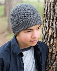 a young boy wearing a knitted hat next to a tree