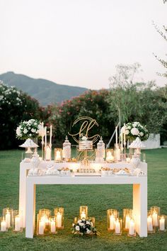 a table topped with lots of candles next to a lush green field covered in flowers