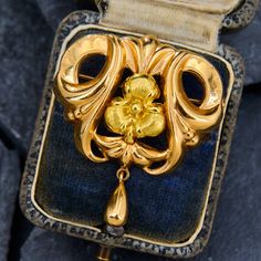 a gold brooch with a flower on it in a blue velvet case, sitting on top of a piece of cloth