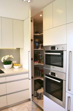 a kitchen with white cabinets and stainless steel ovens in the corner next to an open pantry