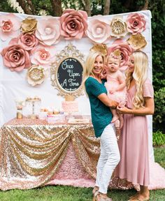 two women and a baby standing in front of a cake table