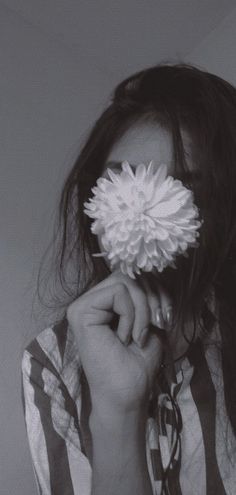 a black and white photo of a woman holding a flower in front of her face