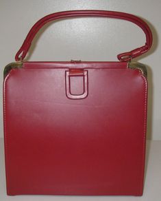 Vintage Handbag Purse Design:  Satchel 1 main compartment with  metal clasp closure and 1 interior zippered pocket with metal zipper with  handle attached to top with gold metal frame Color:   Red Decade:  1950's Material:   Vinyl with black cloth lining Dimensions:  approx.   Strap drop - 5" Height - approx 11" Width - 11" Depth - approx. 2.5" Condition:  unused inside, several slightly lighter streaks in vinyl red,  2 slight rub lines in front side of purse  Handle off-center from years of sto 1950 Handbags, Classic Red Satchel With Gold-tone Hardware, 1950 Purse, 1950s Purse, Red Satchel With Gold-tone Hardware, Purse Design, Vintage Handbag, Purse Handles, Handbag Purse