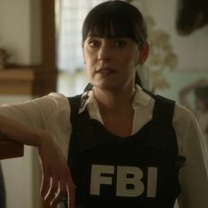 a woman with short black hair wearing a fbi shirt and looking at the camera