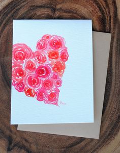 a card with pink and red flowers in the shape of a heart on top of a piece of wood