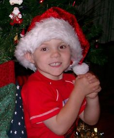 a young boy wearing a santa hat next to a christmas tree