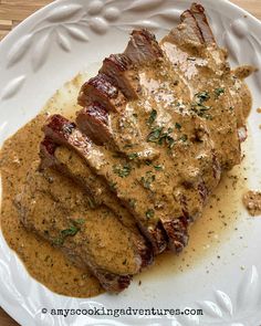 a white plate topped with meat covered in sauce and garnished with parsley