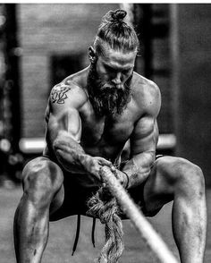 a man with a long beard is tying his shoelaces while squatting on the ground