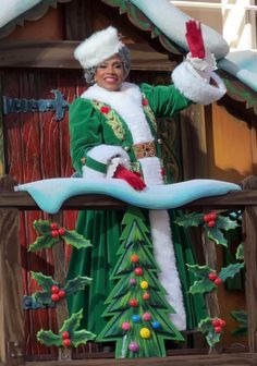 a woman dressed in green and white standing next to a christmas tree