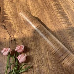 three pink roses sitting on top of a wooden table next to a roll of string