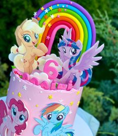 there is a pink cake decorated with little ponys and rainbows on the top