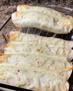 two chicken enchiladas sitting in a glass dish on a counter top, covered with melted cheese