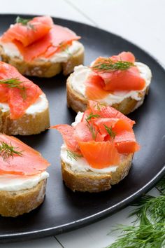 small pieces of bread topped with salmon and cream cheese on a black plate next to fresh dill