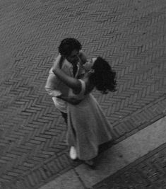 a man and woman are hugging on the side walk in black and white, one is holding the other's head