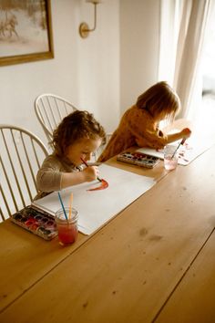 two young children sitting at a table doing arts and crafts